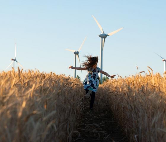 Girl in floral dress running through field towards wind turbines