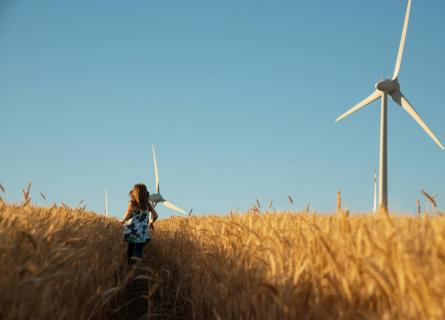 Girl in floral dress is running in corn field with wind turbines