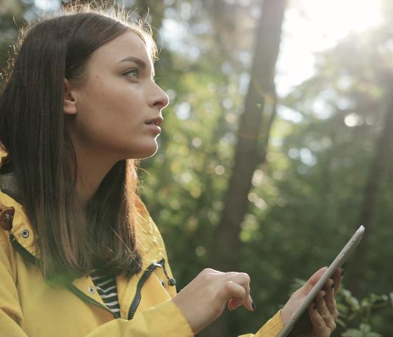 Woman in yellow jacket in forest with tablet